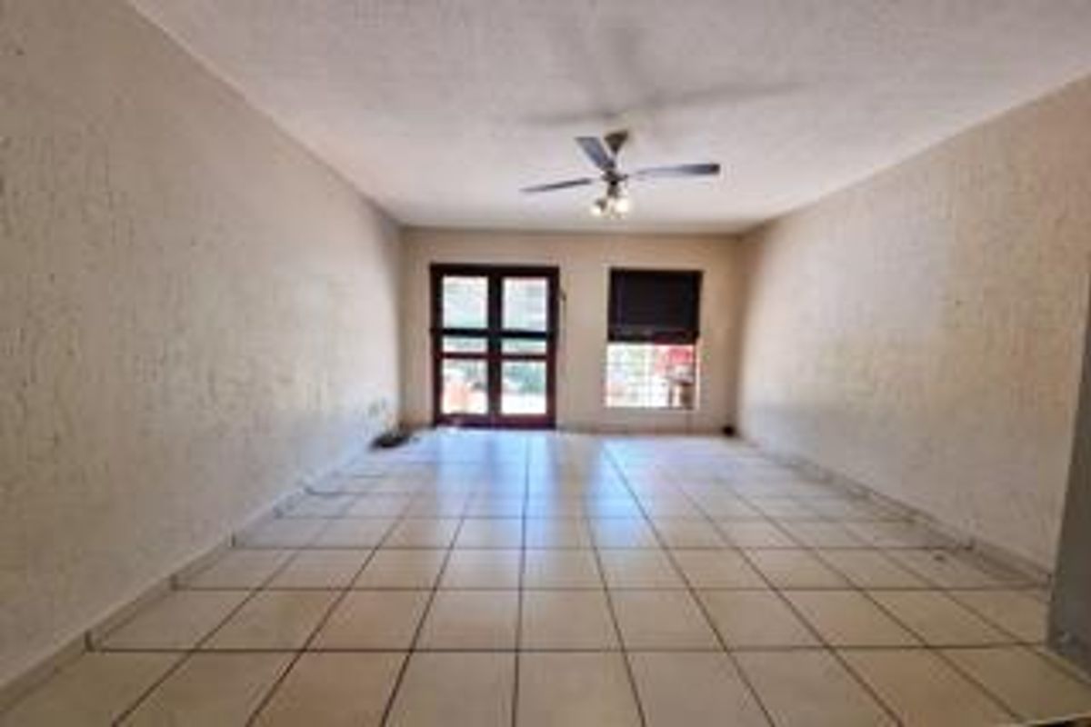 An empty, open-plan living area featuring tiled flooring, a ceiling fan, and access to an outdoor space through a double glass door.
