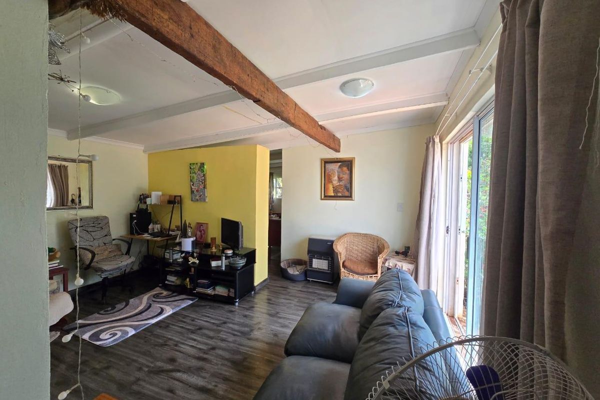 A living room featuring exposed timber ceiling beams, laminate flooring, and sliding glass doors providing access to the outdoor area.