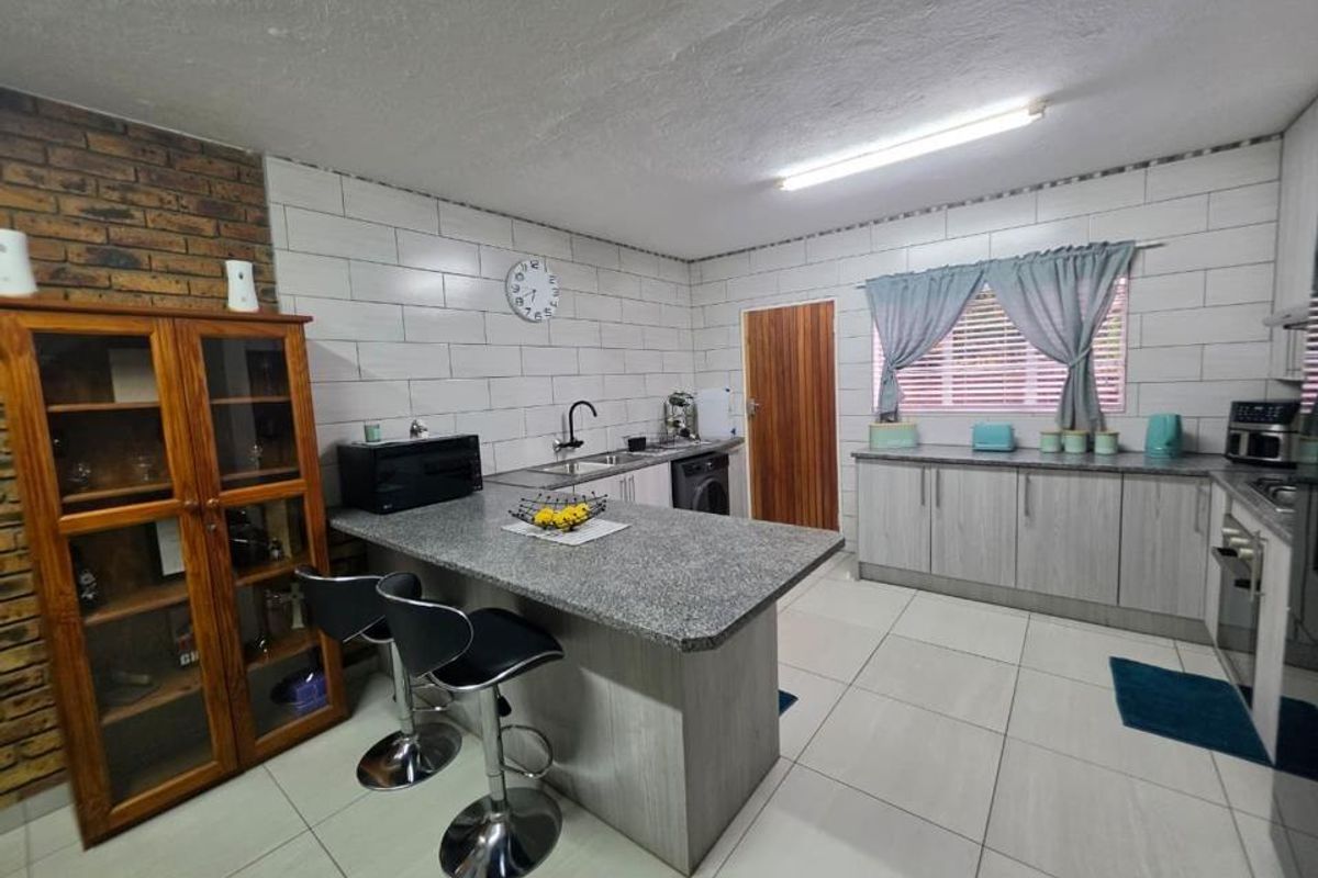 A functional kitchen featuring a central breakfast island, light-toned cabinetry, tiled walls, and integrated appliances, providing a practical workspace for daily cooking.