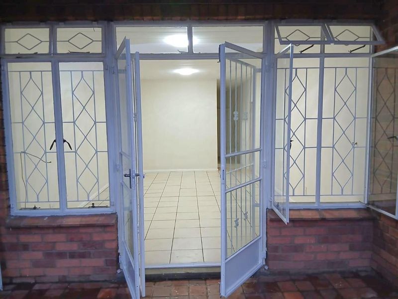 An exterior view of an apartment entrance featuring a security gate, tiled flooring, and brick facade detailing.