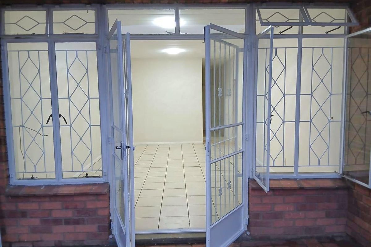 An exterior view of an apartment entrance featuring a security gate, tiled flooring, and brick facade detailing.