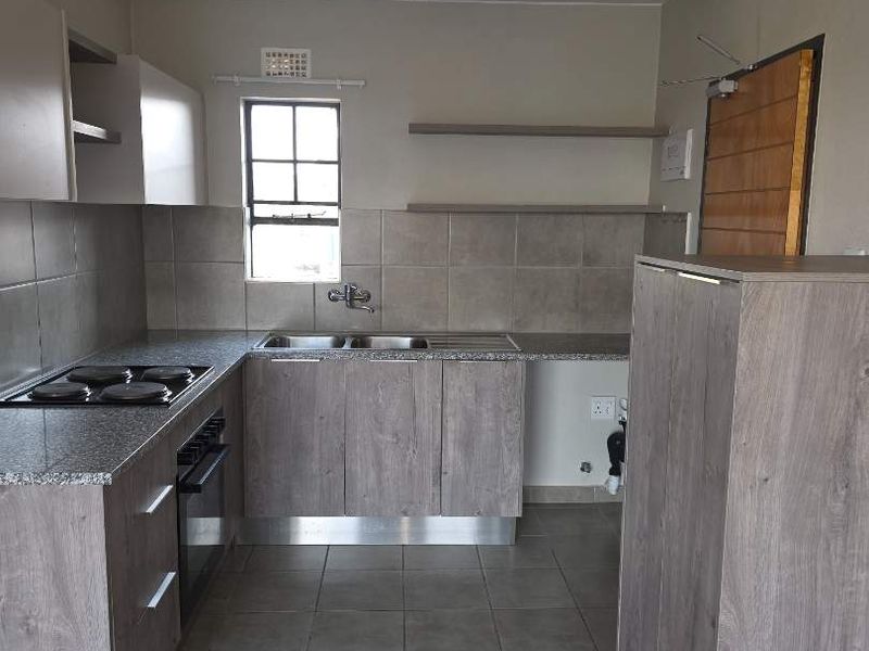 A functional kitchen featuring wood-look cabinetry, granite countertops, built-in oven and hob, and tiled flooring, offering a clean and practical workspace.