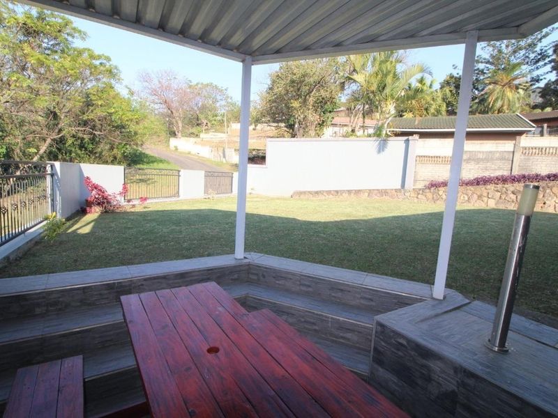 A covered outdoor patio featuring built-in tiled seating, overlooking a private lawn and garden area with perimeter walling.