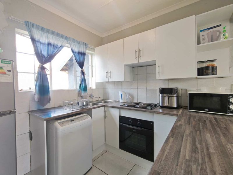 Compact kitchen featuring white cabinetry, laminate countertops, built-in oven, electric hob, and tiled backsplash with a functional layout.