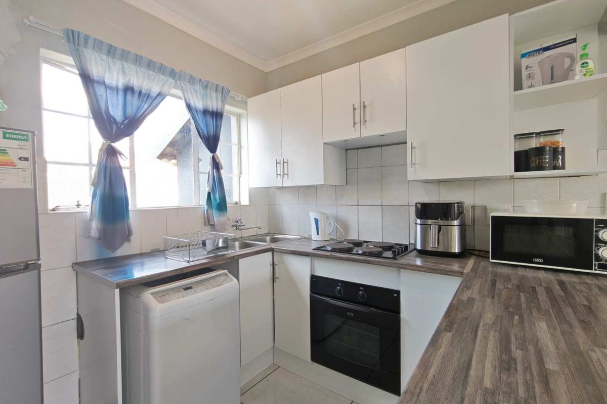 Compact kitchen featuring white cabinetry, laminate countertops, built-in oven, electric hob, and tiled backsplash with a functional layout.