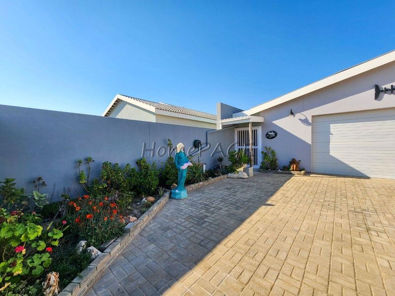 Front exterior view of the property featuring a paved driveway, garage access, and a landscaped garden bed along the boundary wall.