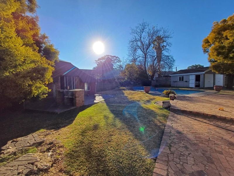 Spacious rear garden featuring a swimming pool, paved patio area, and a built-in brick braai, complemented by a detached garage.