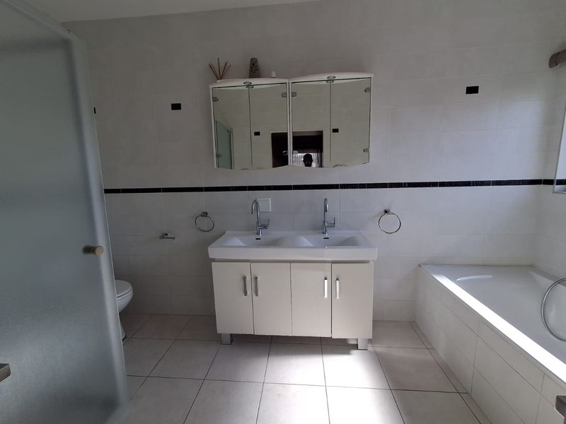 A functional bathroom featuring a double vanity with a built-in medicine cabinet, tiled walls, a built-in bathtub, and a separate shower enclosure.