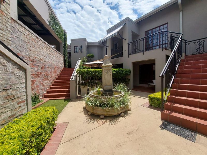 A charming rear courtyard featuring a central stone fountain, tiled staircases, and wrought iron balcony railings, creating a private and well-maintained outdoor living space.