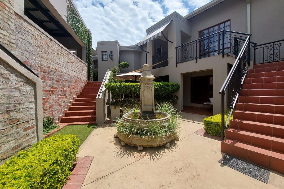 A charming rear courtyard featuring a central stone fountain, tiled staircases, and wrought iron balcony railings, creating a private and well-maintained outdoor living space.