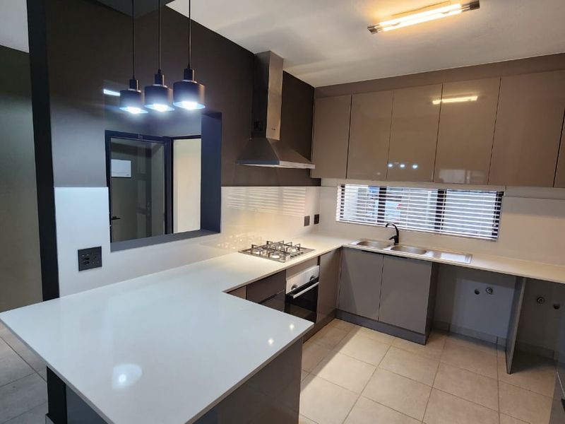 Modern kitchen featuring high-gloss cabinetry, quartz countertops, gas hob, extractor fan, and tiled flooring in a clean, contemporary layout.