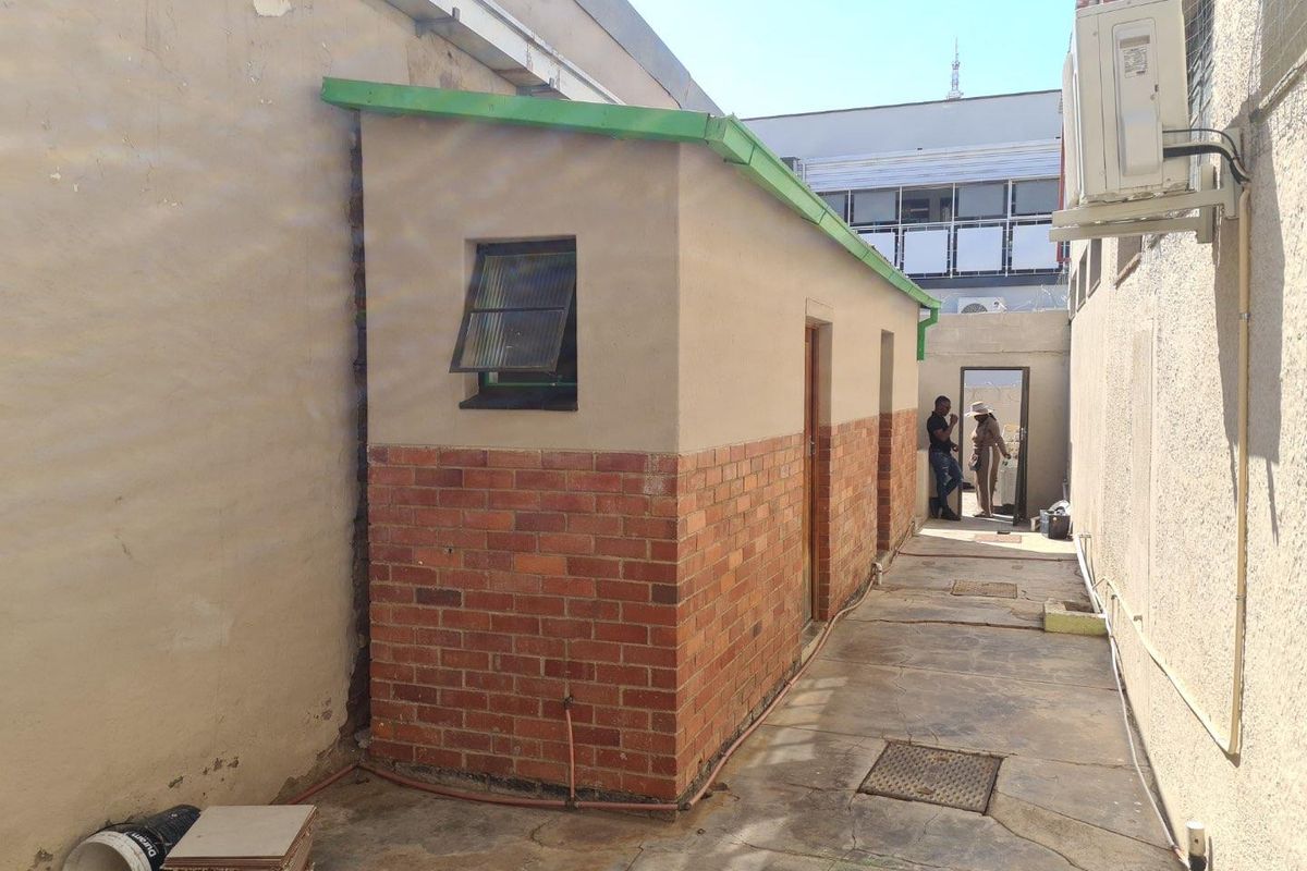 Rear exterior service alley featuring brick masonry walls, concrete paving, and an external air conditioning unit.