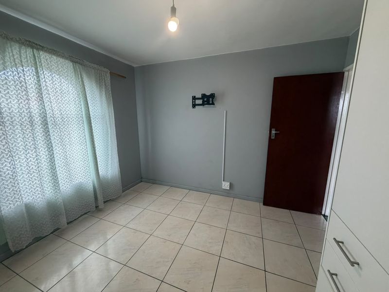 A clean, empty bedroom featuring tiled flooring, a built-in wardrobe, and a wall-mounted TV bracket, ready for personalization.