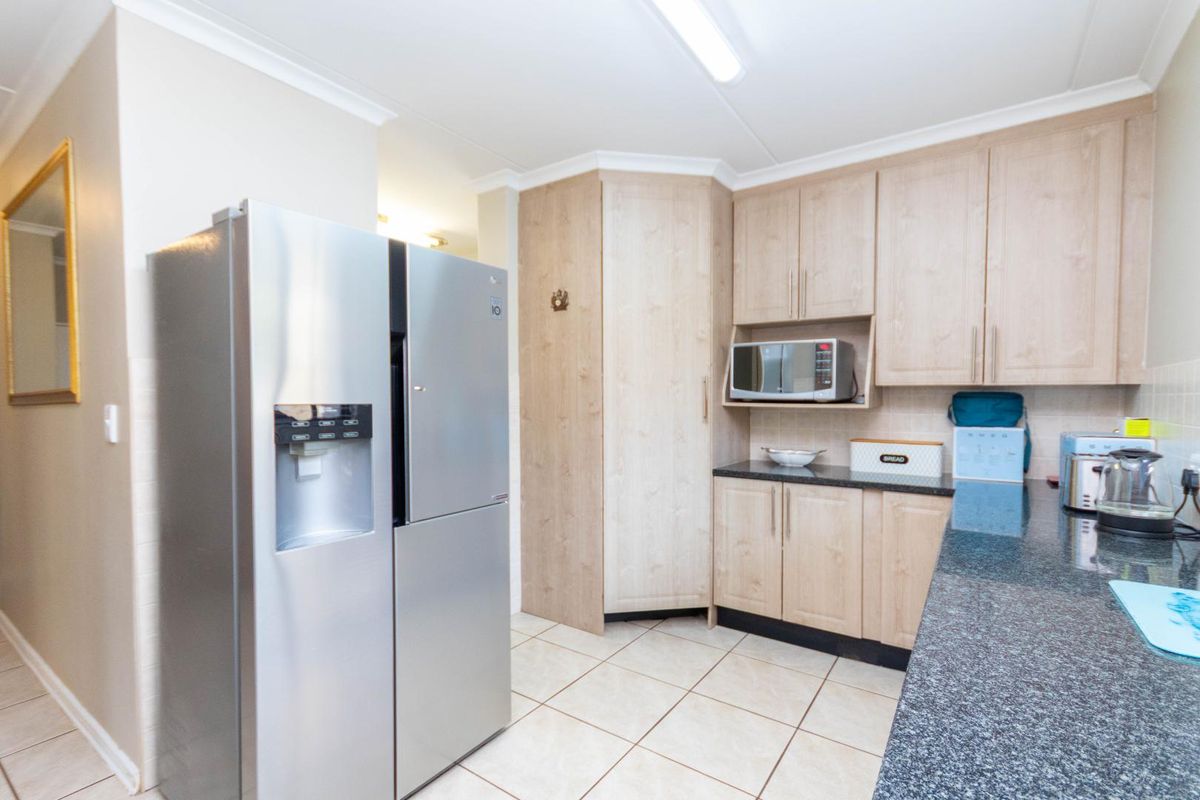 A functional kitchen featuring light wood-finish cabinetry, dark granite countertops, built-in microwave space, and neutral ceramic floor tiles.