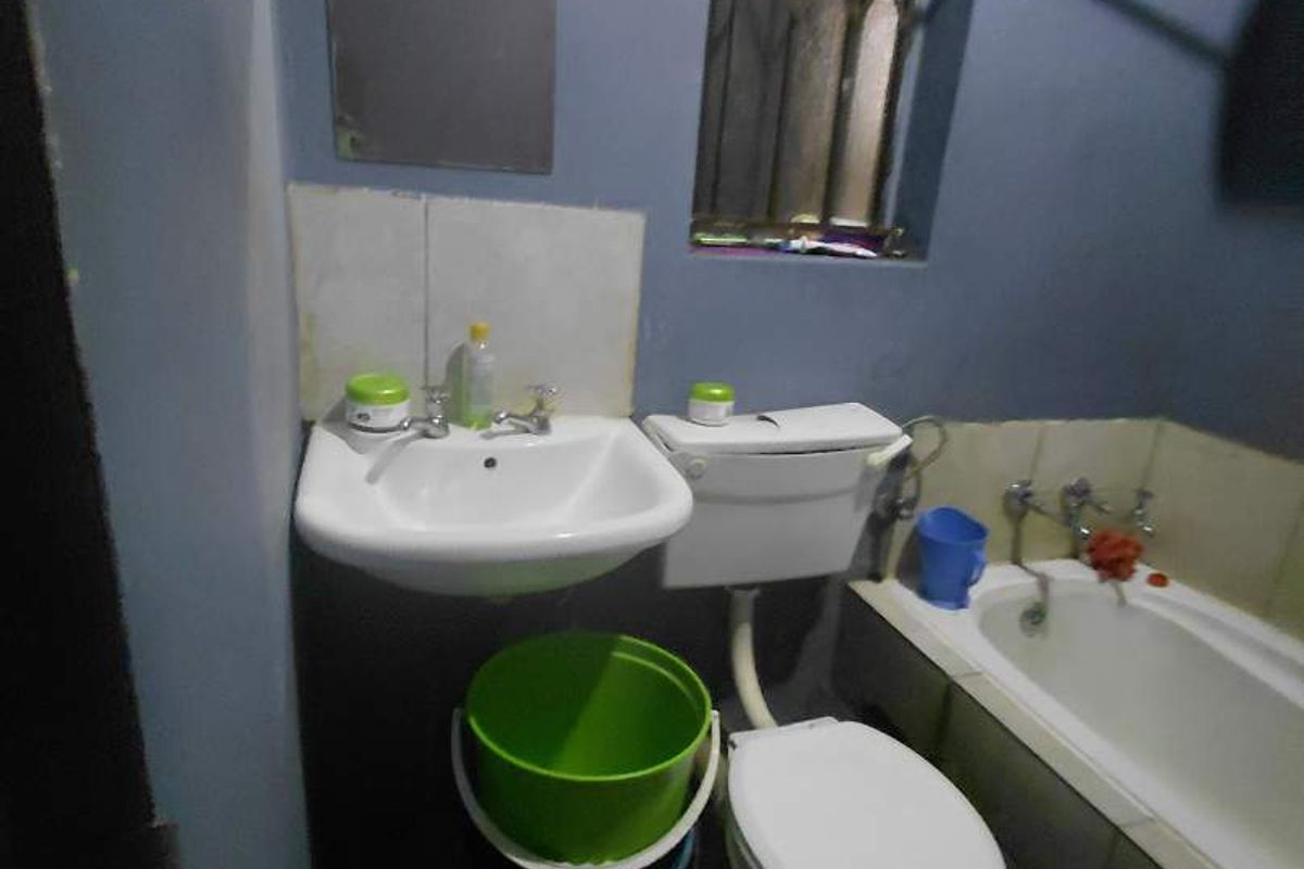 A compact bathroom featuring a standard bathtub, pedestal basin, and toilet, with a window fitted with security bars.