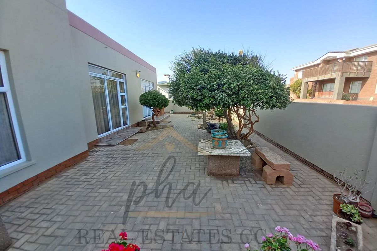 A paved rear courtyard area featuring a low boundary wall and direct access to the home through sliding glass doors.