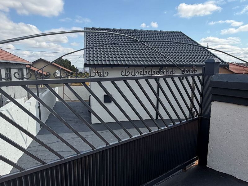 A view of the property entrance featuring a modern metal driveway gate, paved driveway, and a well-maintained tiled roof structure.