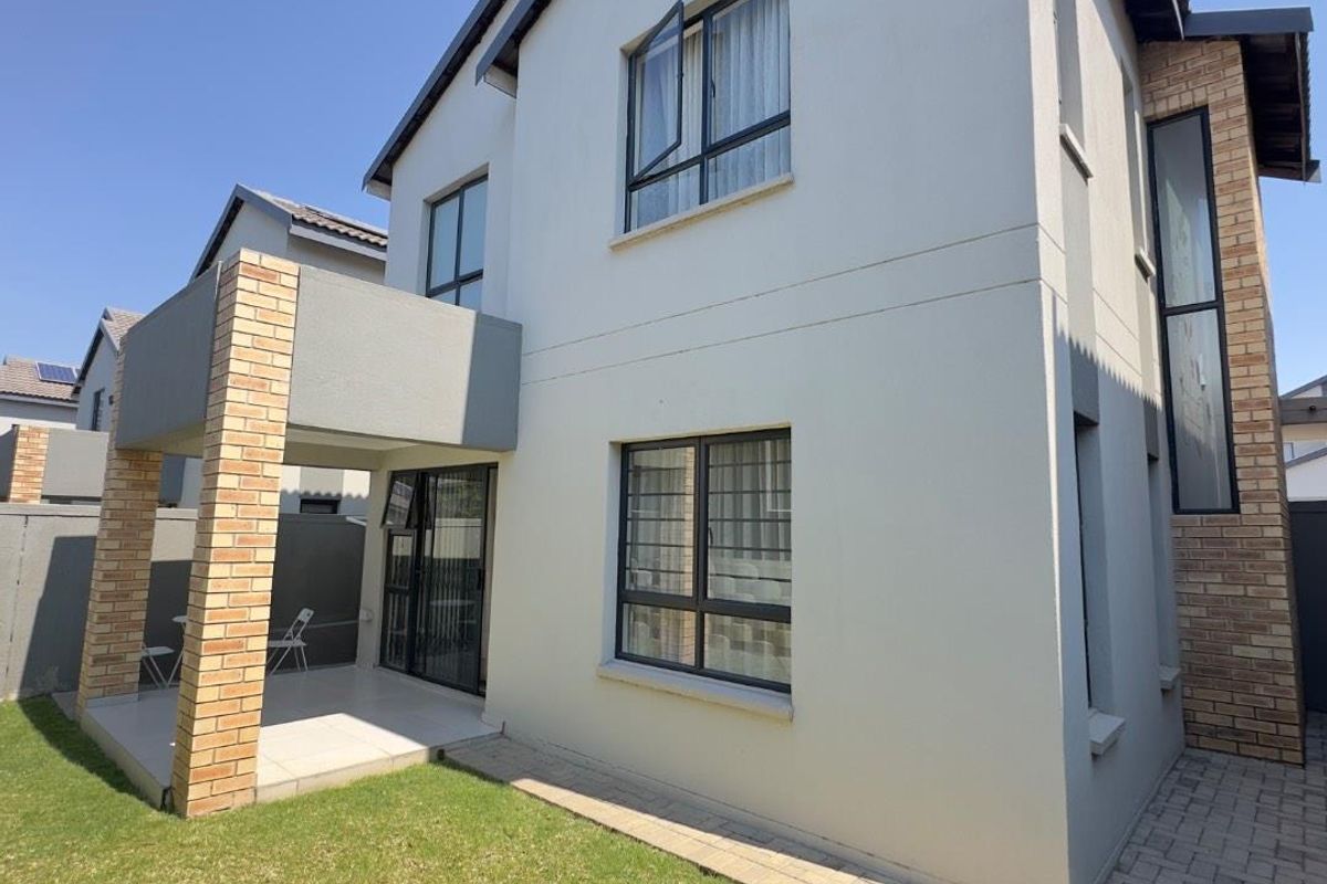 Rear view of a modern townhouse featuring a covered patio, brick accents, aluminium window frames, and a well-maintained garden area.