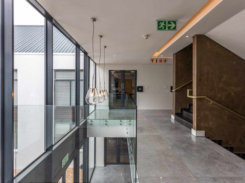 Modern commercial hallway featuring large glass windows, tiled flooring, a glass balustrade, and a staircase with a metal handrail.