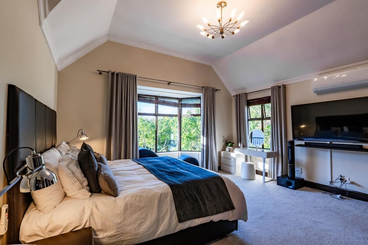 Spacious bedroom featuring a vaulted ceiling, large bay window with garden views, and a wall-mounted air conditioning unit.