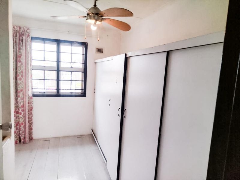 A bedroom featuring built-in cupboards, a ceiling fan, and laminate flooring, offering a functional space with potential for cosmetic updates.