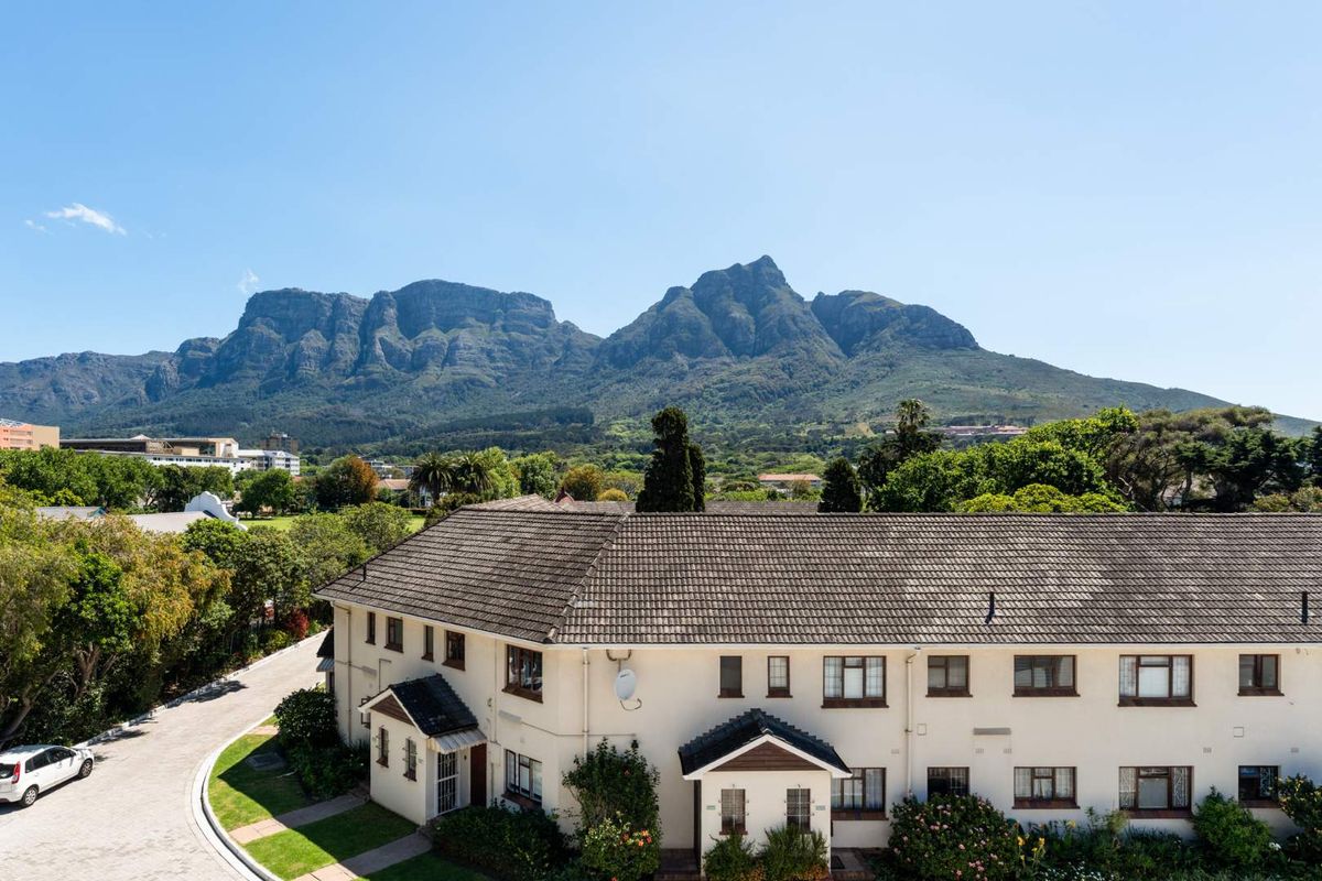 Aerial view of the apartment complex featuring a tiled roof, paved driveway, and surrounding landscaped gardens with a scenic mountain backdrop.