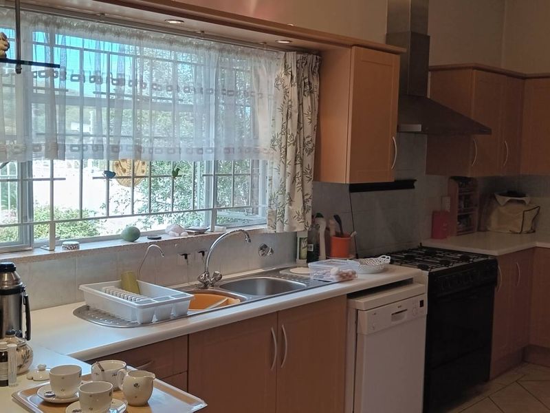 A functional kitchen featuring light wood-tone cabinetry, a gas stove with extractor fan, stainless steel sink, and tiled flooring with natural light.