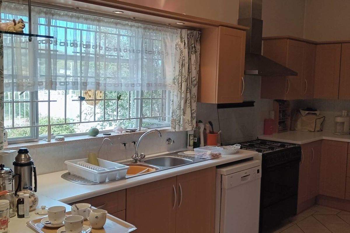 A functional kitchen featuring light wood-tone cabinetry, a gas stove with extractor fan, stainless steel sink, and tiled flooring with natural light.