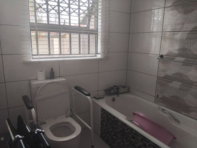 A functional bathroom featuring a bathtub, toilet, and tiled wall finishes, equipped with a window for natural light and ventilation.