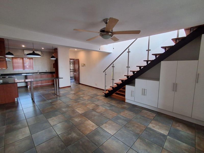 Spacious open-plan living area featuring tiled floors, a modern staircase with glass balustrade, built-in under-stair storage, and an integrated kitchen.