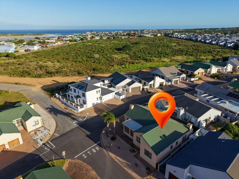 Aerial view of a residential estate featuring multiple houses with tiled roofs, paved driveways, and coastal proximity.