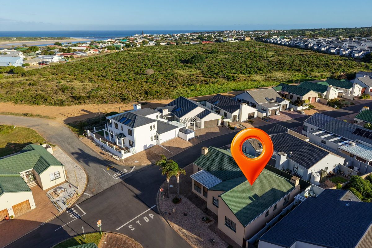 Aerial view of a residential estate featuring multiple houses with tiled roofs, paved driveways, and coastal proximity.