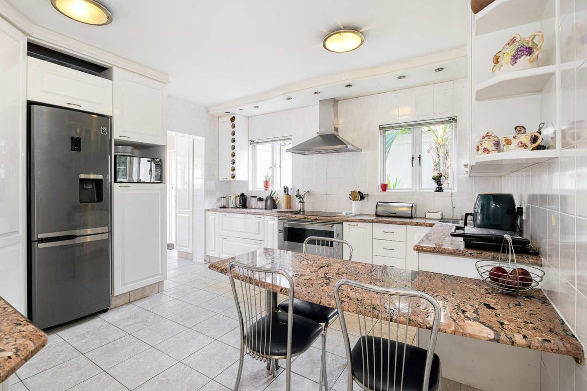 A functional kitchen featuring white cabinetry, granite countertops, a breakfast bar, and stainless steel appliances, including a built-in oven and extractor fan.
