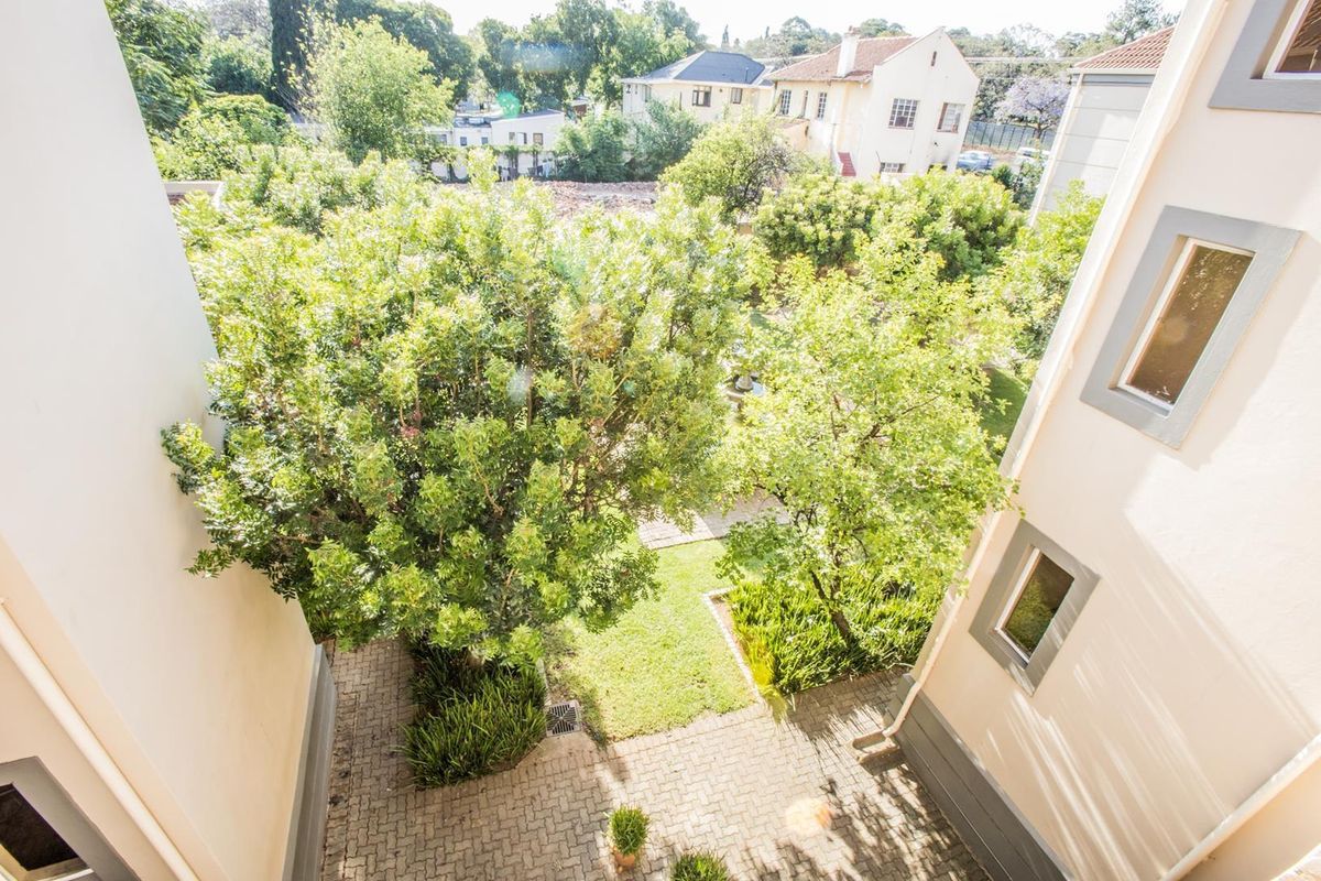An elevated view looking down into a private courtyard garden featuring paved walkways, established trees, and landscaped garden beds between townhouse structures.