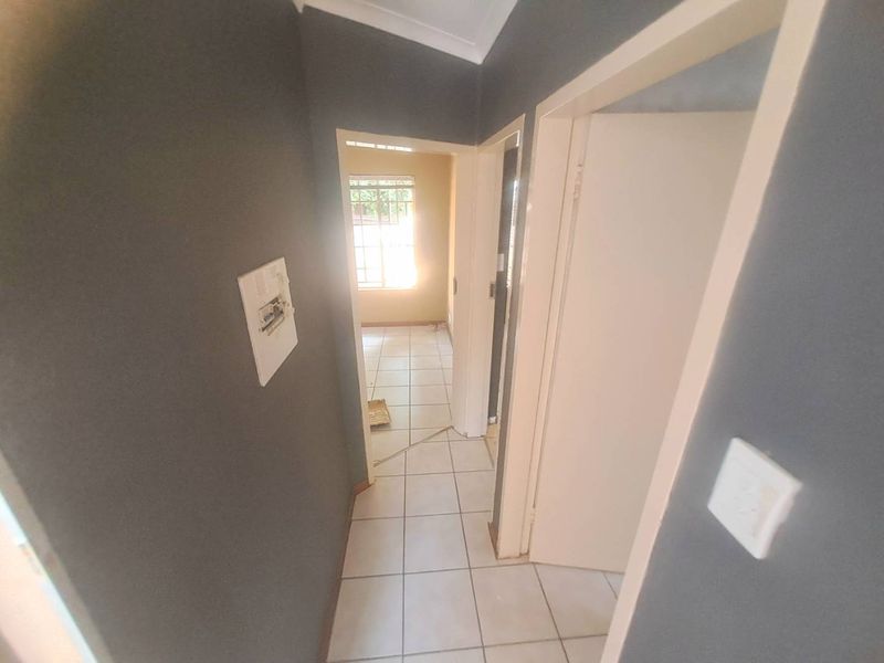 A vacant hallway featuring tiled flooring, dark grey walls, and access to adjacent rooms, showing signs of wear on finishes.