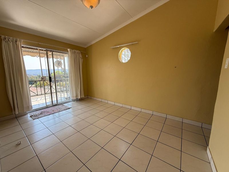 An empty living room featuring tiled flooring, a unique circular window, and sliding glass doors that open to a balcony with scenic views.