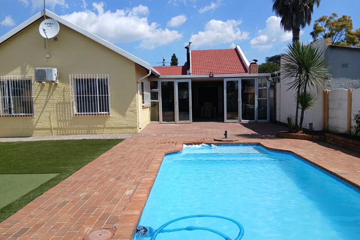 Rear view of the property featuring a swimming pool, paved patio area, and a well-maintained garden with artificial lawn.