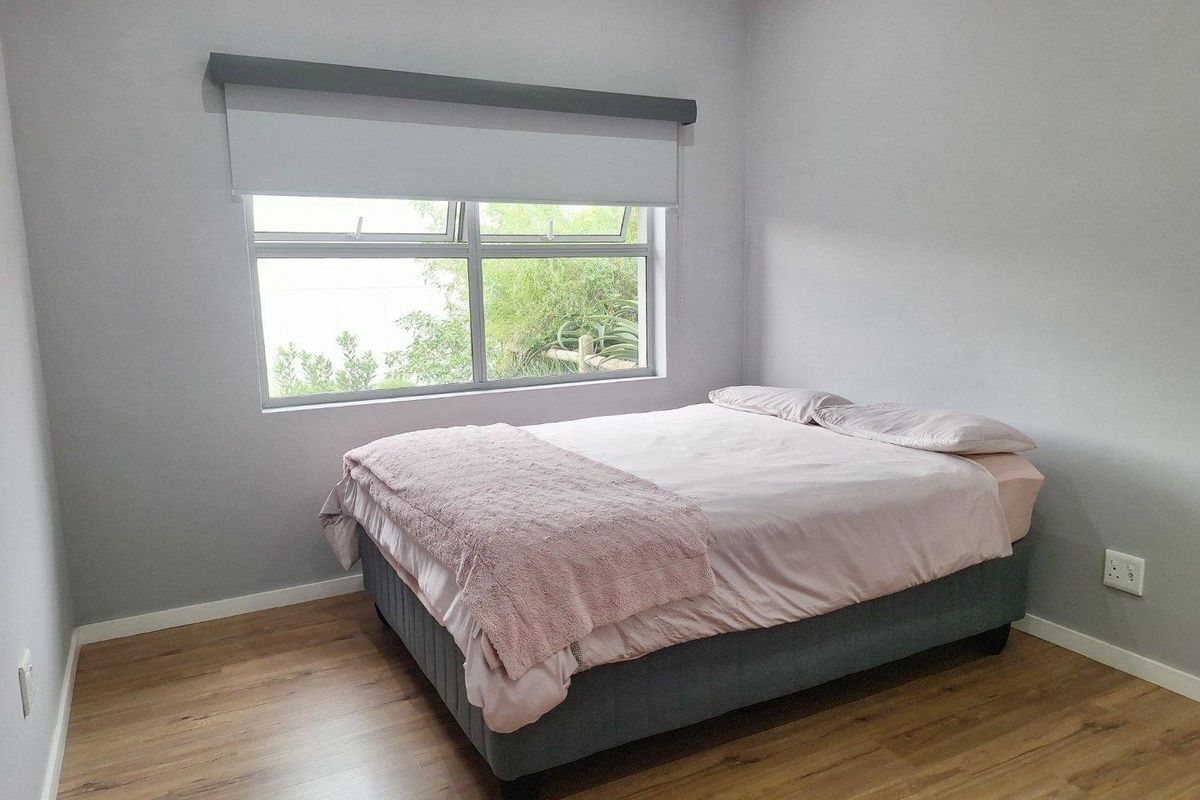 A well-maintained bedroom featuring modern laminate flooring, neutral grey walls, and a large window with a fitted roller blind.