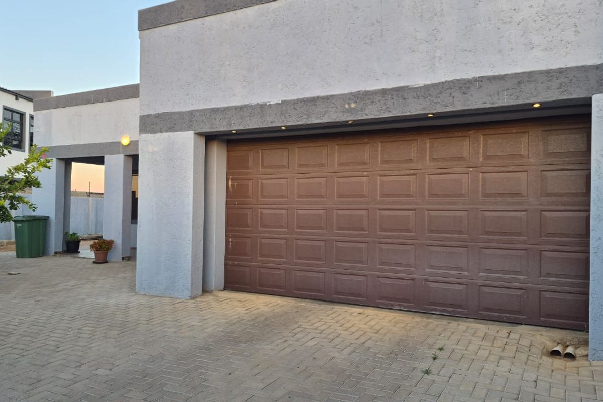 A modern residential garage featuring a brown sectional door, recessed exterior lighting, and a paved driveway area.