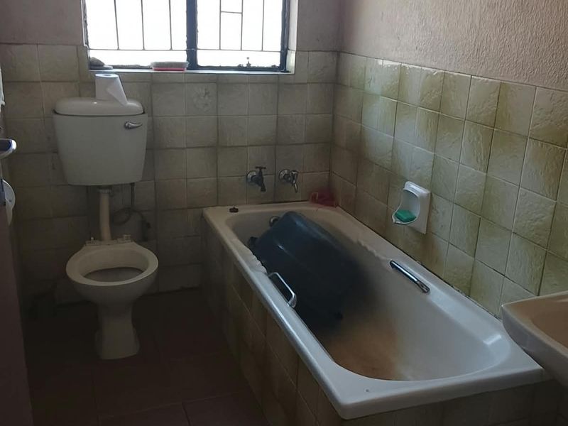 A dated bathroom featuring a built-in bathtub, toilet, and wall-mounted basin, requiring cosmetic updates and refurbishment of the tiled surfaces.