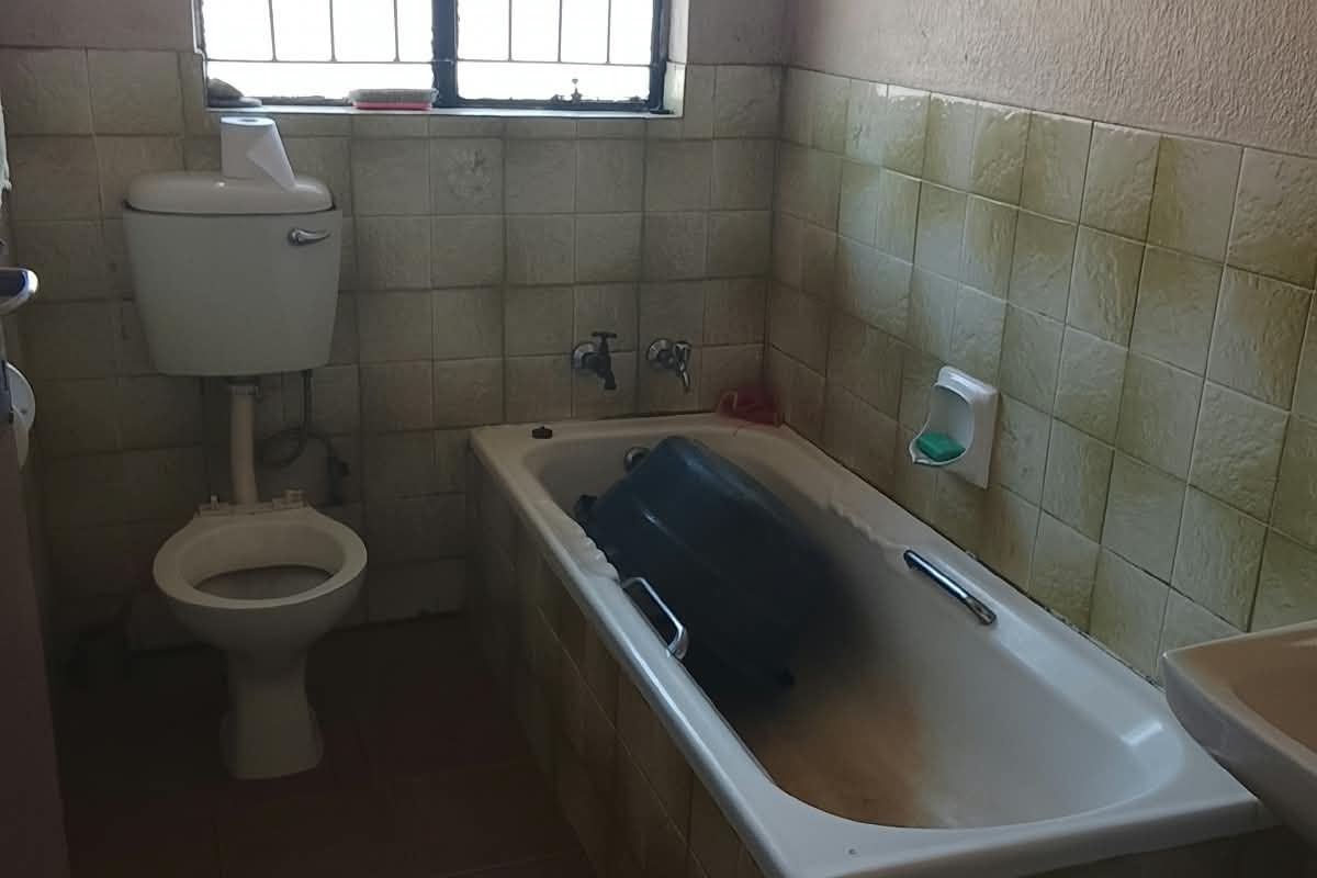 A dated bathroom featuring a built-in bathtub, toilet, and wall-mounted basin, requiring cosmetic updates and refurbishment of the tiled surfaces.
