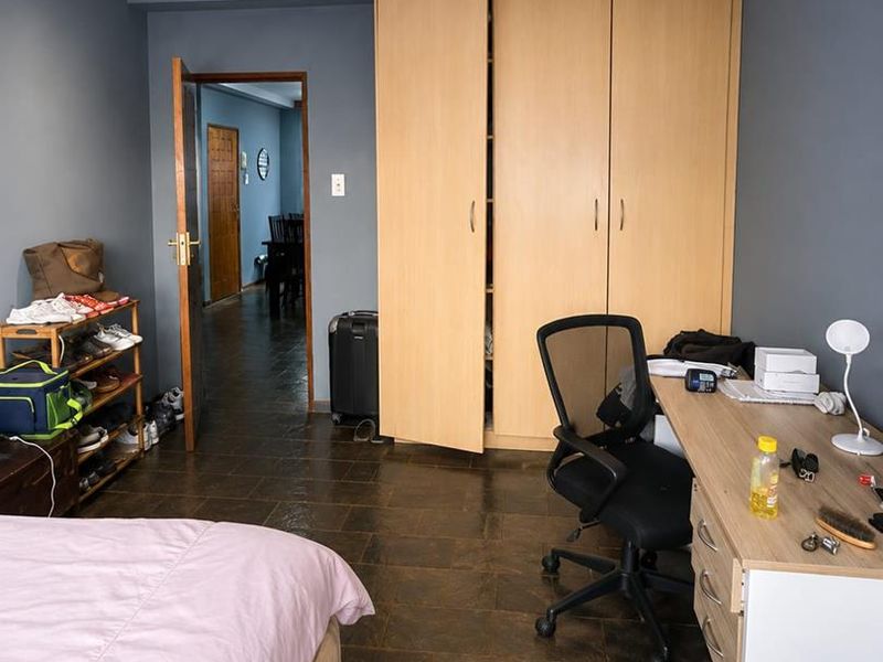 A bedroom featuring dark tiled flooring, recessed downlighting, and a large built-in wooden wardrobe, offering a functional space with neutral wall tones.
