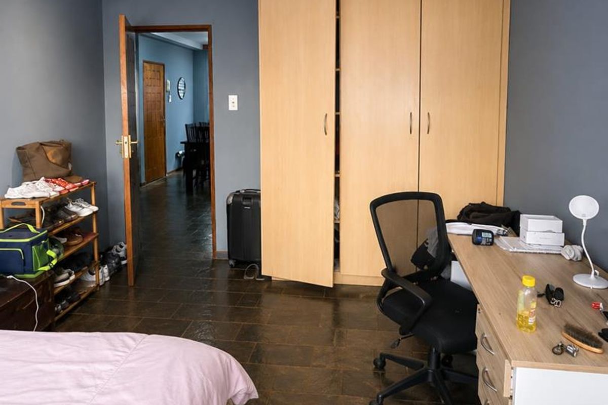 A bedroom featuring dark tiled flooring, recessed downlighting, and a large built-in wooden wardrobe, offering a functional space with neutral wall tones.