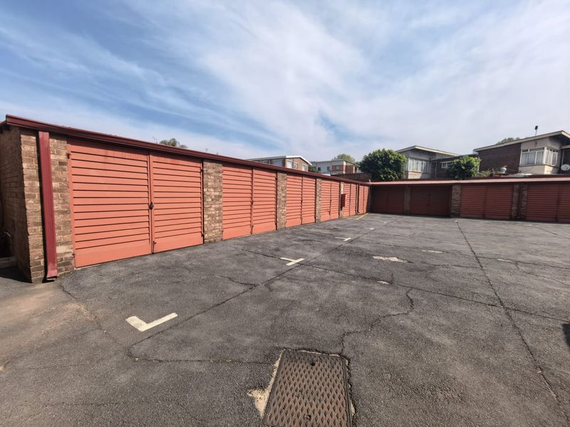 A row of secure metal garage units with an asphalt parking area featuring visible surface cracking.