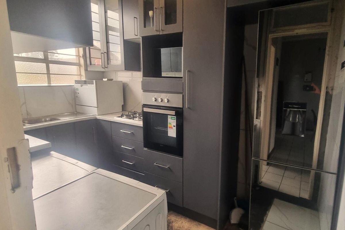 A functional kitchen featuring dark grey cabinetry, a built-in oven, gas hob, and stainless steel sink with a tiled backsplash.