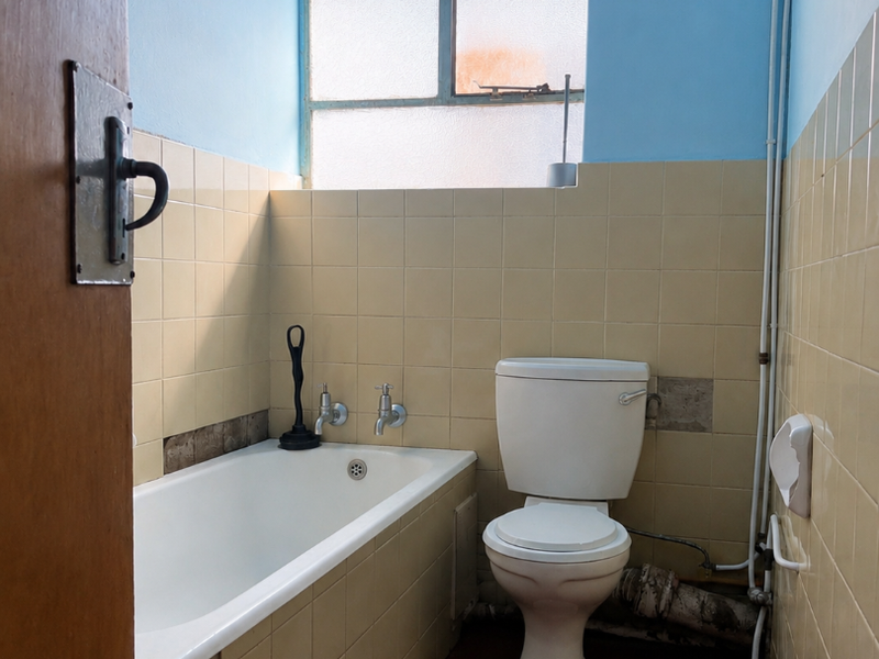 A dated bathroom featuring a standard bathtub, toilet, and tiled walls. The space requires modernization of fixtures and finishes.