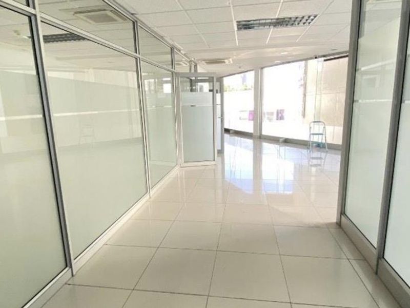 Modern, bright office space featuring glass partition walls, polished tiled flooring, and a suspended ceiling with integrated lighting and air conditioning.