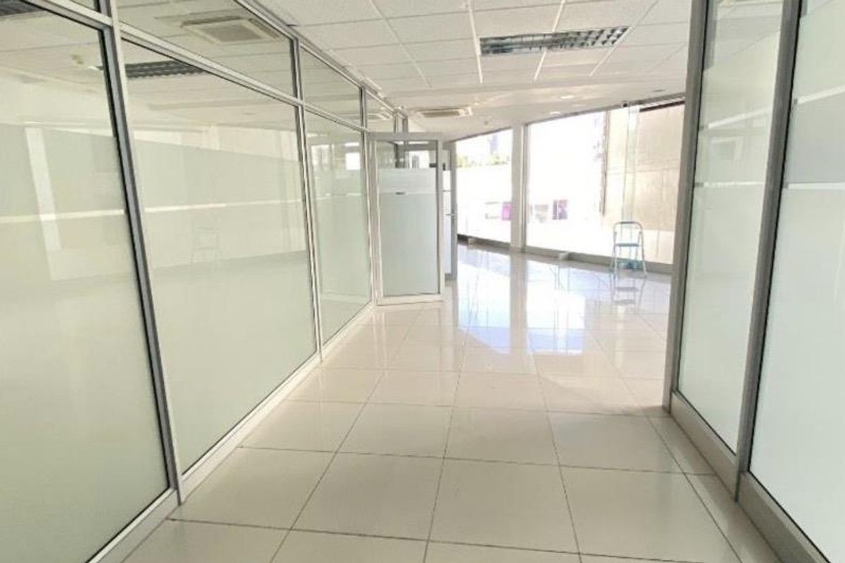 Modern, bright office space featuring glass partition walls, polished tiled flooring, and a suspended ceiling with integrated lighting and air conditioning.