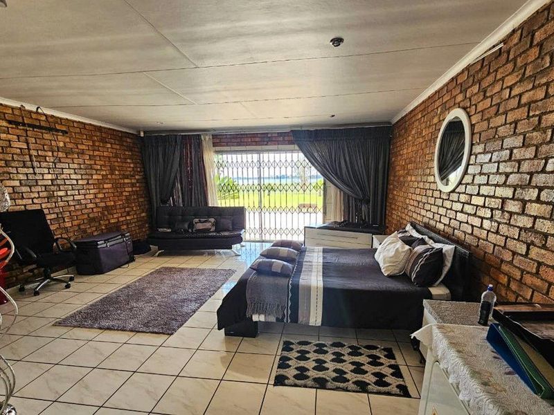 Spacious bedroom featuring exposed brick walls, tiled flooring, and a sliding glass door with security gate providing access to the exterior.