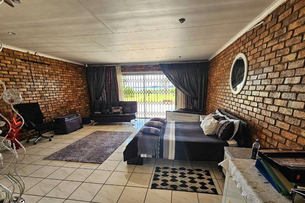 Spacious bedroom featuring exposed brick walls, tiled flooring, and a sliding glass door with security gate providing access to the exterior.